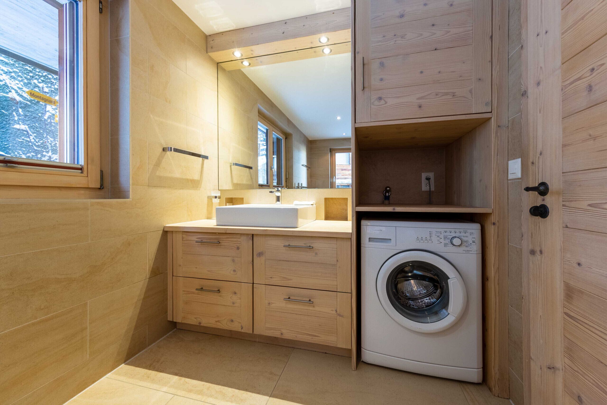 Une salle de bain moderne et compacte, dotée de meubles en bois, d’un lave-linge encastré et d’un grand miroir.