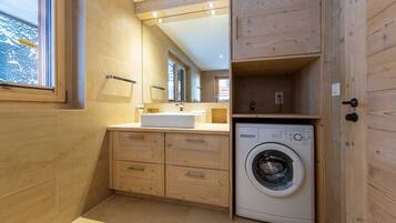 Une salle de bain moderne et compacte, dotée de meubles en bois, d’un lave-linge encastré et d’un grand miroir.