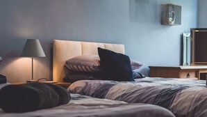 Et soveværelse med to senge, et sengebord, en lampe og en højttaler på væggen.