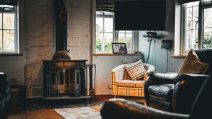 En hyggelig stue med pejs, lædersofa og et tv monteret på væggen.