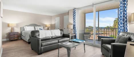 A modern hotel room with a bed, two sofas, a coffee table, and a balcony with a view.
