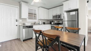 A modern kitchen with white cabinets, a stainless steel refrigerator, and a wooden dining table with four chairs. - Beautiful Beach and Tennis Studio #3305 (Bonita Springs)