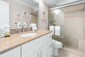 A modern bathroom with a granite countertop, a white sink, a glass-enclosed shower, and a toilet.