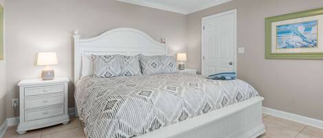 A bedroom with a white bed, two bedside tables with lamps, a door, and a framed picture on the wall.