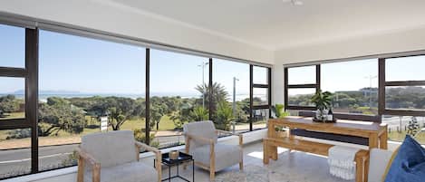A spacious living area with large windows, a wooden coffee table, and a sofa with a blue pillow.
