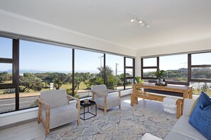 A spacious living area with large windows, a wooden coffee table, and a sofa with a blue pillow. - Cisterama 102 (Cape Town)
