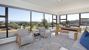 A spacious living area with large windows, a wooden coffee table, and a sofa with a blue pillow. - Cisterama 102 (Cape Town)