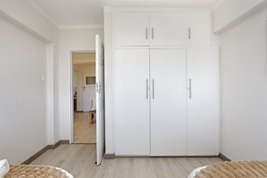 A bedroom with a large wardrobe, a bed, and a door leading to another room. - Cisterama 102 (Cape Town)
