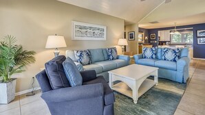A living room with a ceiling fan, two sofas with patterned cushions, a coffee table, and a potted plant.