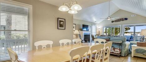 A spacious living area with a dining table and chairs, a television, and a ceiling fan.