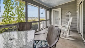 A covered patio with a ceiling fan, a table with chairs, and a view of the water.