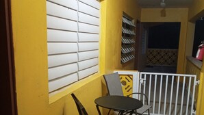 A small outdoor seating area with a table and chairs, a window with blinds, and a white railing.