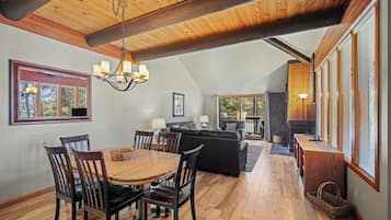 A spacious living area with a wooden ceiling, a dining table with chairs, a sofa, and a fireplace.
