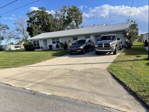 Uma casa de dois andares com garagem, entrada para carros e dois SUVs estacionados.