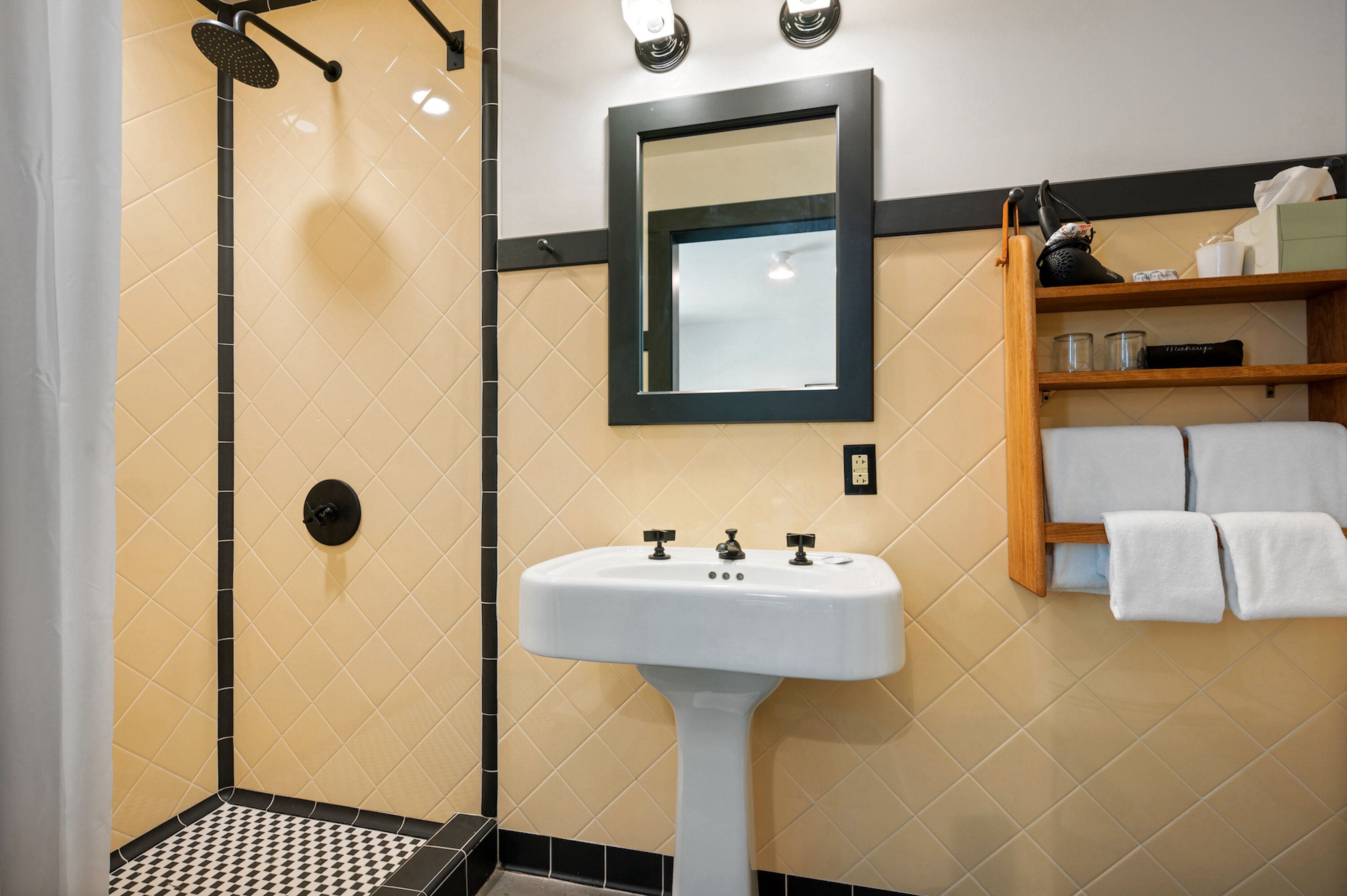 A bathroom with a white sink, a mirror, a shower, and a shelf with towels.