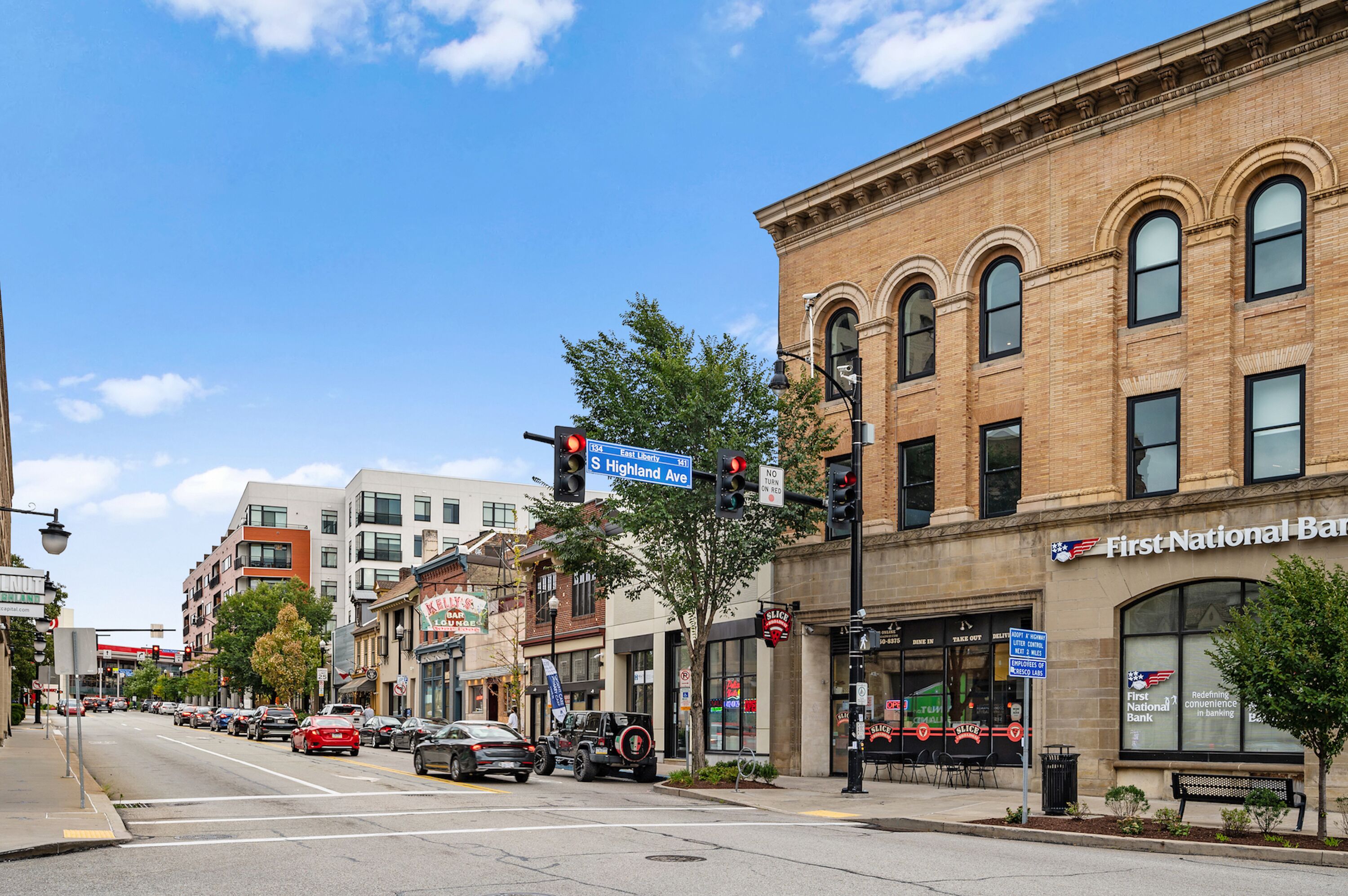 A street view with a First National Bank building, cars on the road, and various storefronts.