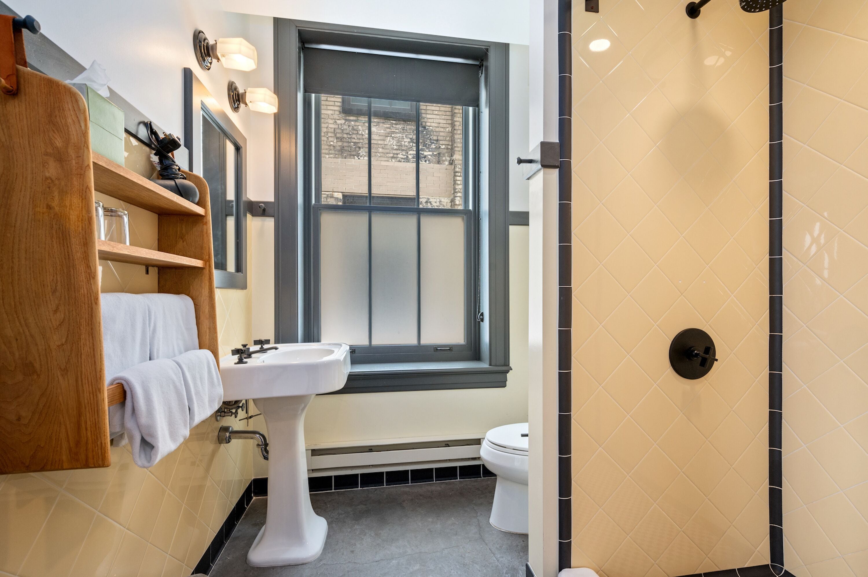 A bathroom with a white sink, a toilet, a window with a view, and a shower area.