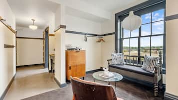 A room with a large window, a wooden cabinet, a bench with cushions, and a glass table.