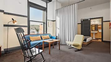 Camera d'albergo moderna con un divano blu, una poltrona a dondolo, un tavolino e un letto con comodino.