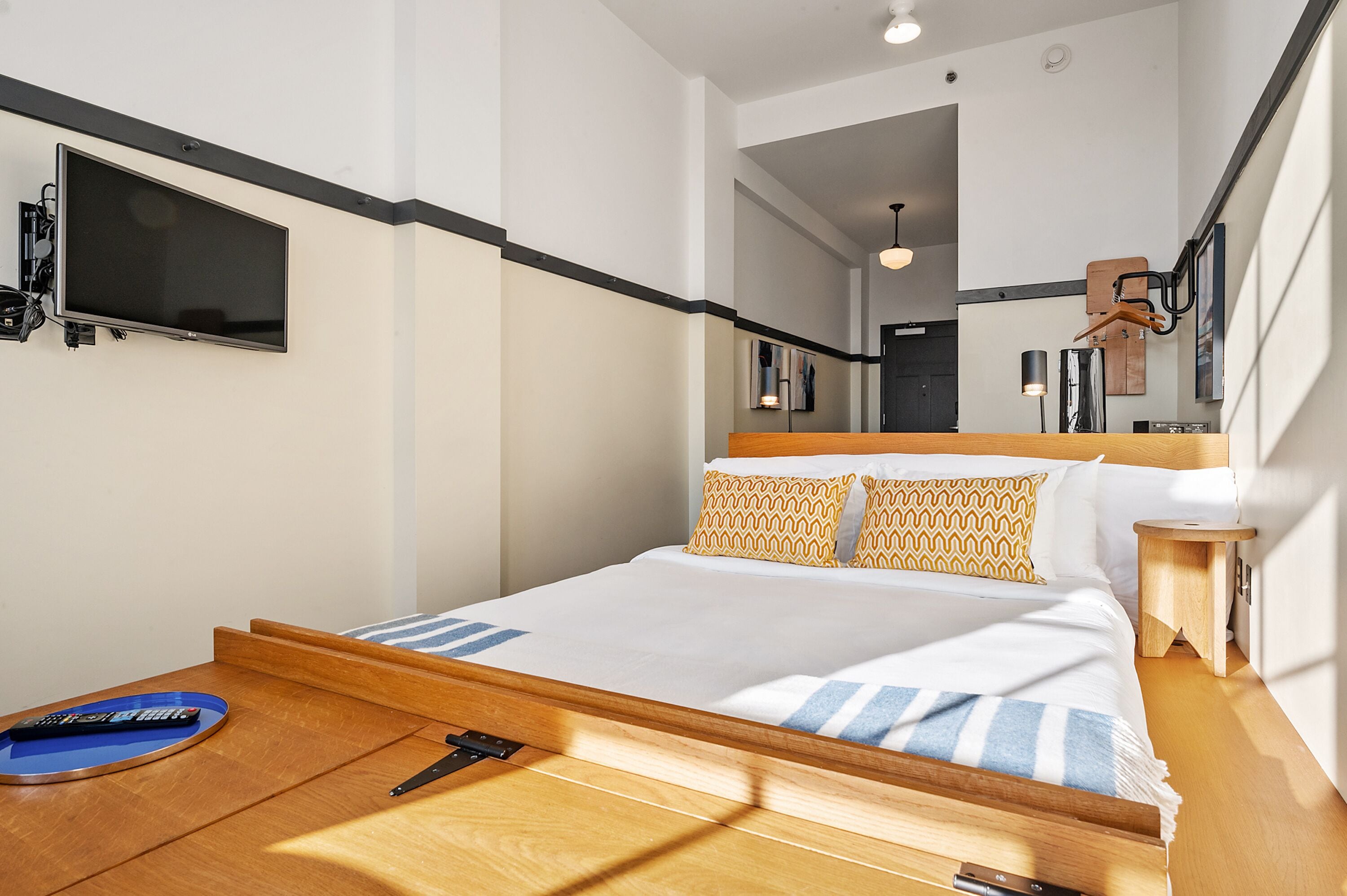 A modern hotel room with a bed, bedside table, and a mounted TV.