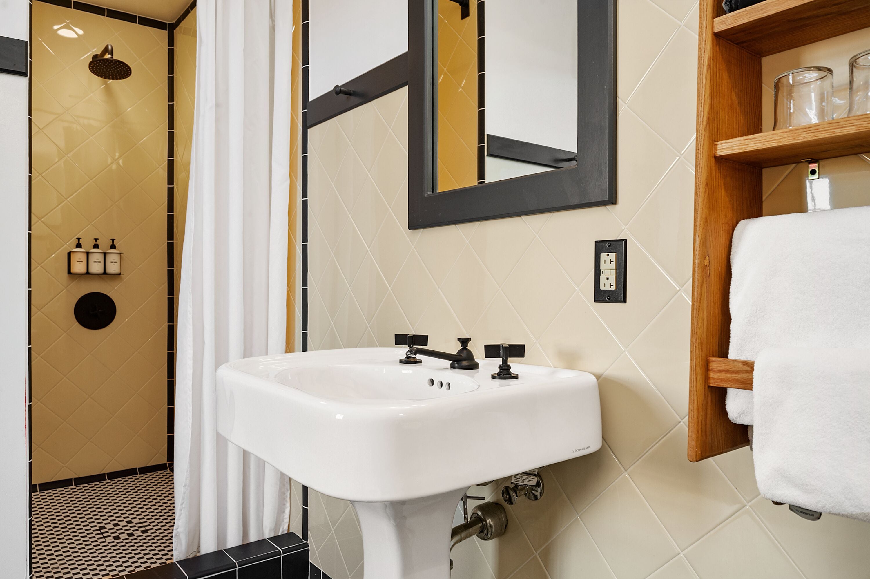 A bathroom with a white sink, a mirror, a shower, and a shelf with toiletries.