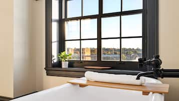 A bathroom with a bathtub, a window with a view, a towel, and a potted plant.