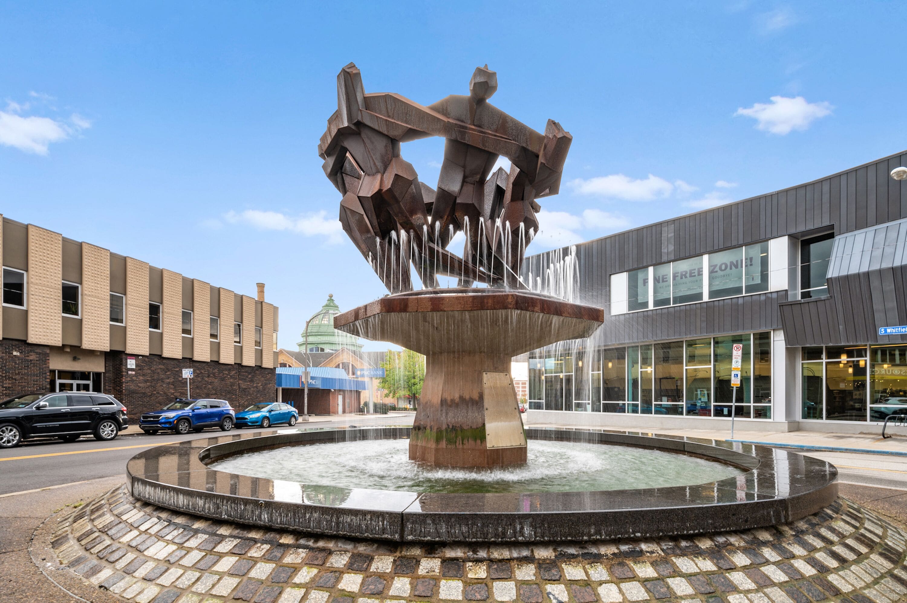 A modern building with a large glass facade and a central water feature with a metal sculpture.