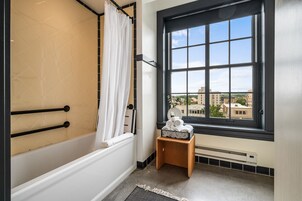 A bathroom with a bathtub, a window with a view of buildings, a towel rack, and a heater.