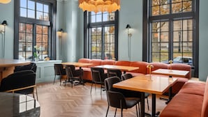 Un restaurante con suelo de espiga, ventanas amplias y una zona central con asientos naranjas y mesas.