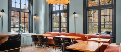 A restaurant with a herringbone floor, large windows, and a central seating area with orange booths and tables.