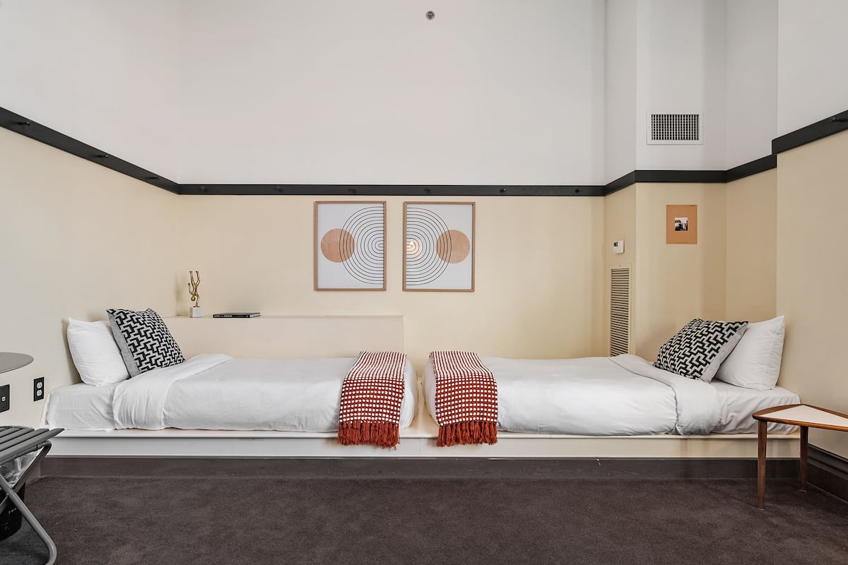 A modern hotel room with a large bed, a small table, and two framed artworks on the wall.