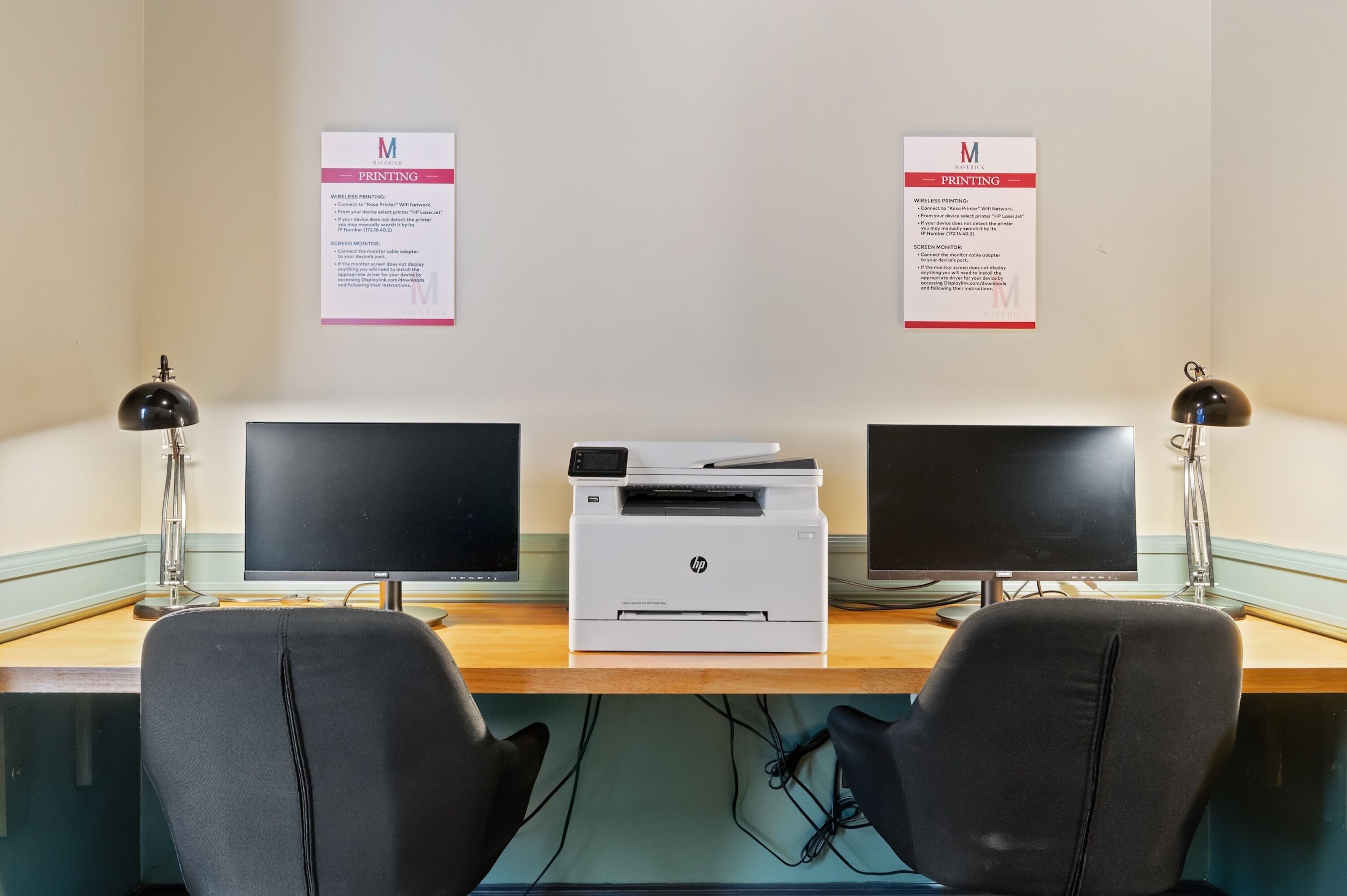 A workspace with two HP printers, two monitors, and two black office chairs.