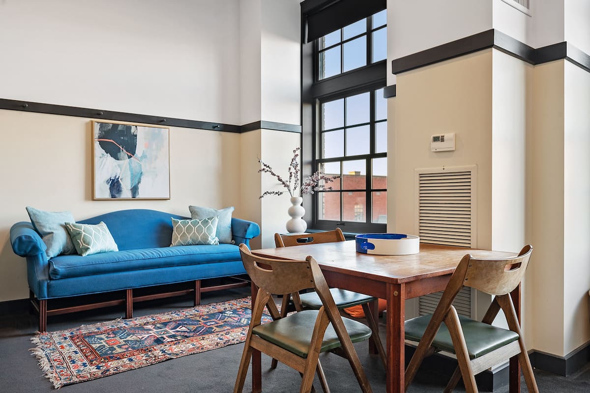 A modern living room with a blue sofa, wooden dining table, and chairs.