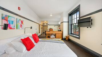Habitación de hotel con una cama grande, un escritorio, un televisor y obras de arte en la pared.