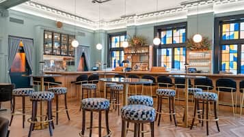 A bar area with multiple stools, a bar counter, and a large window with colorful stained glass.