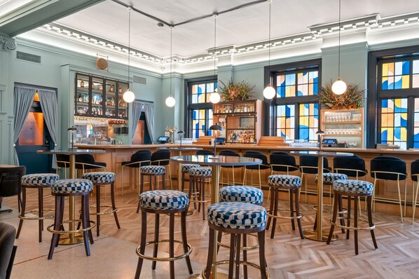 Una zona de bar con varios taburetes, una barra y un amplio ventanal con vidrieras de colores.