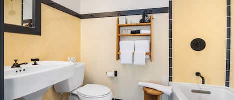 A modern bathroom with a toilet, sink, and bathtub. There is a shelf with towels and toiletries.