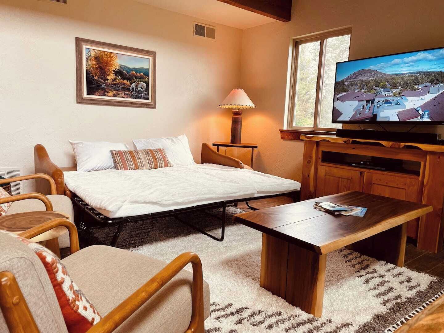 Una habitación de hotel con una cama, un escritorio de madera, un televisor y un cuadro en la pared.