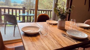Un coin repas avec une table en bois dressée pour deux personnes, une plante en pot et une vue sur l’extérieur.