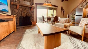 Un salon chaleureux avec une cheminée en pierre, des meubles en bois et une grande fenêtre donnant sur l’extérieur.