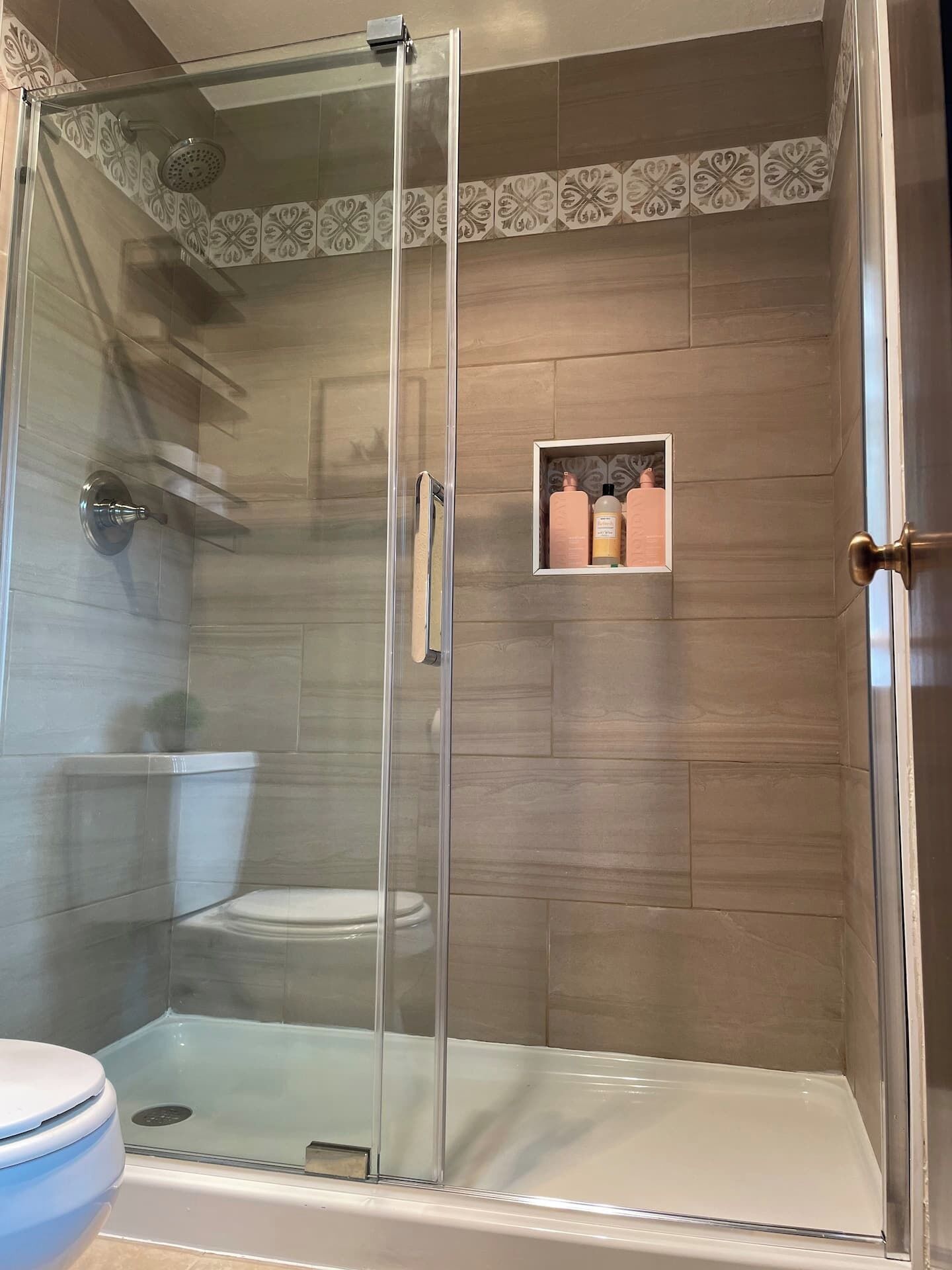 Une cabine de douche fermée par des parois en verre, avec des toilettes et une étagère contenant des articles de toilette.