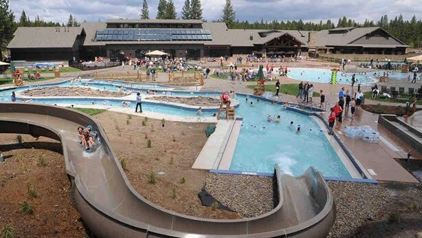 Un parc aquatique doté de plusieurs piscines et de toboggans, entouré d’immeubles et d’arbres.