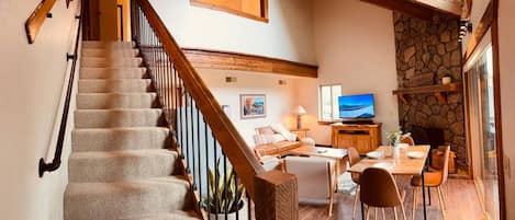 A staircase leading to a living area with a stone fireplace, a television, and a dining table.
