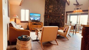 Un salon chaleureux avec une cheminée en pierre, des meubles en bois et un téléviseur diffusant un paysage pittoresque.