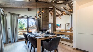 A dining area with a wooden table set for four, large windows with curtains, and a view of mountains. - JATOBA - Chalet with a jacuzzi and cinema corner (Chamonix-Mont-Blanc)