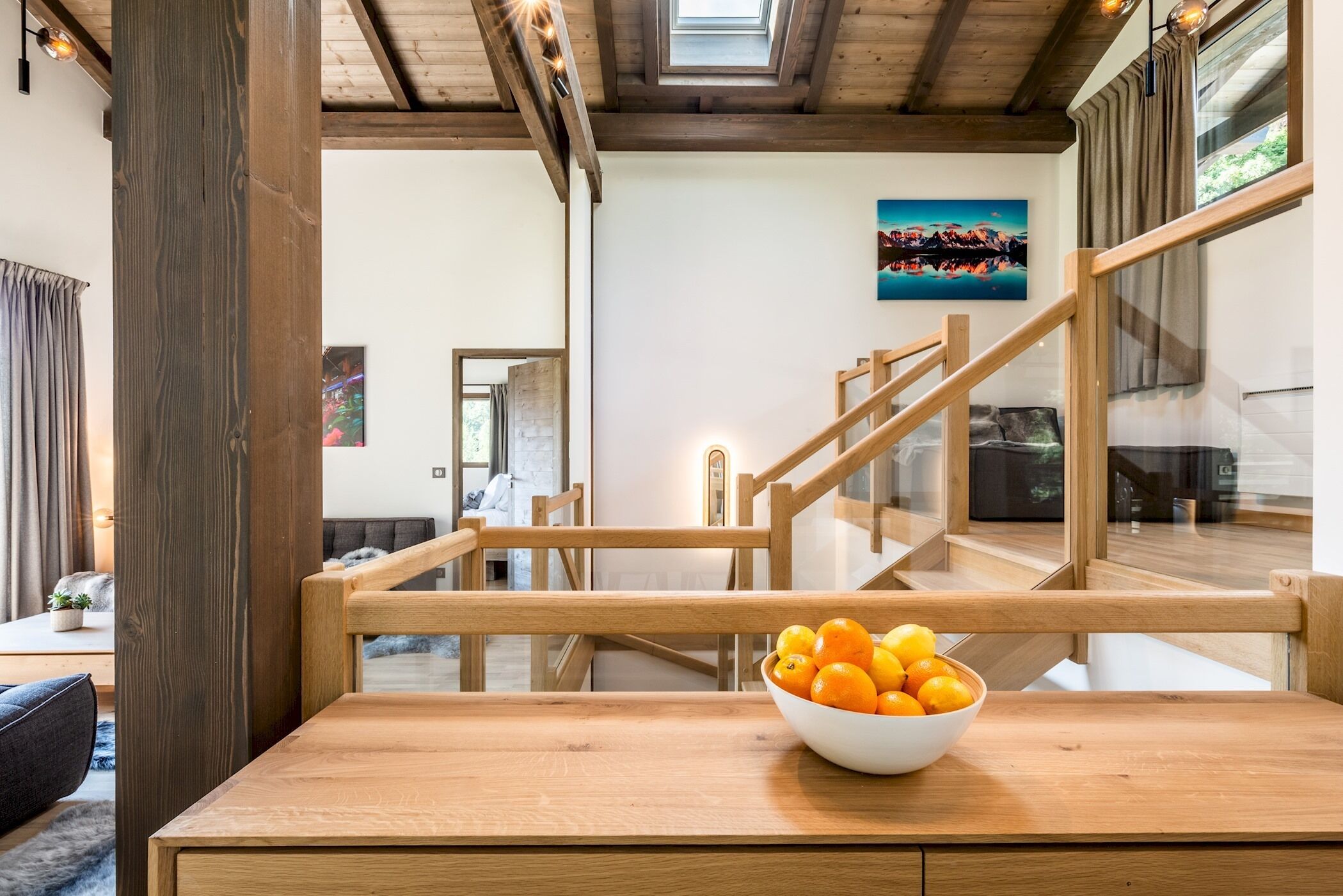 Un interno moderno con una scala in legno, una ciotola di arance su un tavolo e un quadro appeso al muro.
