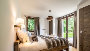 A modern bedroom with a wooden bed, two bedside lamps, and a view of a garden through large windows. - JATOBA - Chalet with a jacuzzi and cinema corner (Chamonix-Mont-Blanc)