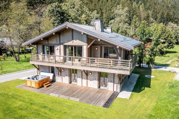 Une cabane moderne en bois, dotée d’un balcon, d’un jacuzzi et offrant une vue sur la forêt environnante.