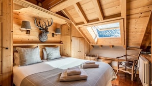 Une chambre confortable dans un chalet en bois, avec un lit, des oreillers, une lampe, une décoration représentant une tête de cerf, une chaise et une lucarne.