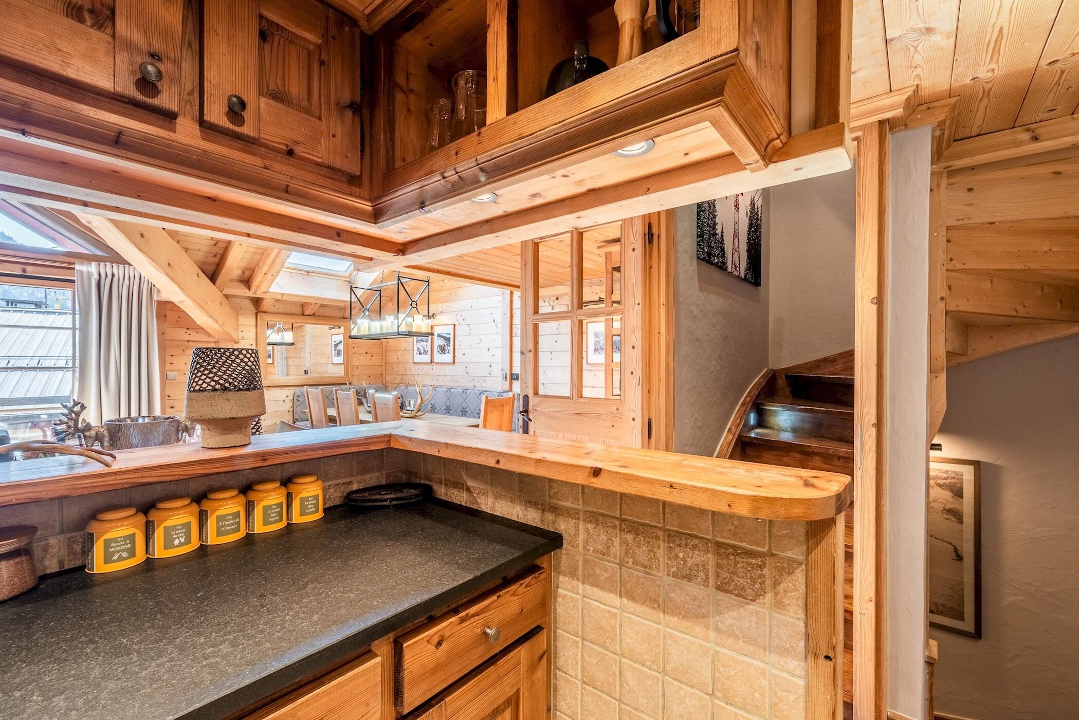 Una cucina in legno con piano di lavoro nero, mobili impiallacciati e zoccolo piastrellato.